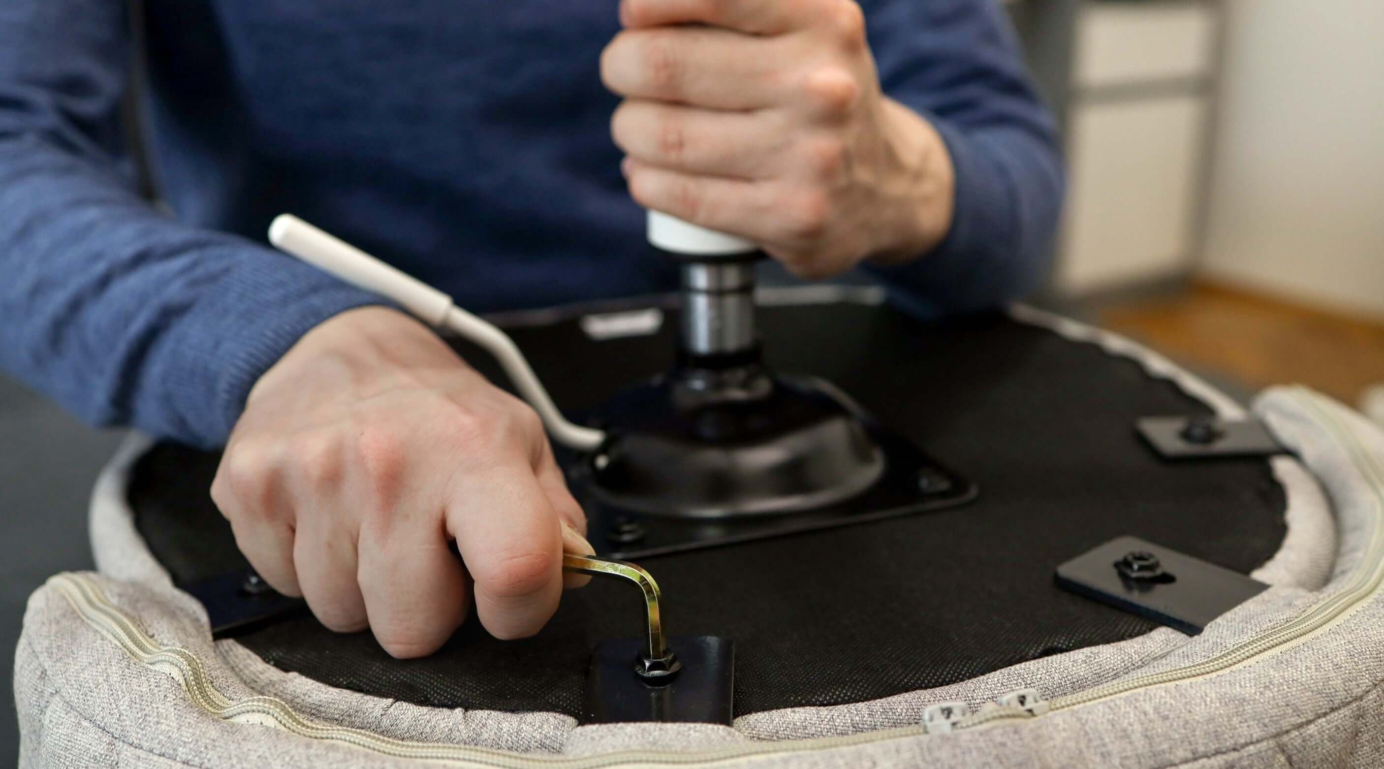 Person using an Allen key to tighten or loosen screws on the underside of a chair.