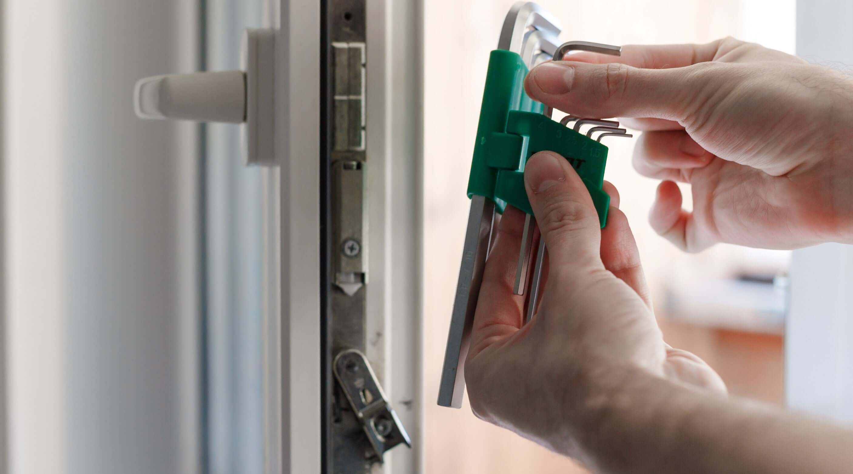 Person using a green holder with Allen wrenches to fix a door lock, demonstrating DIY tool usage.