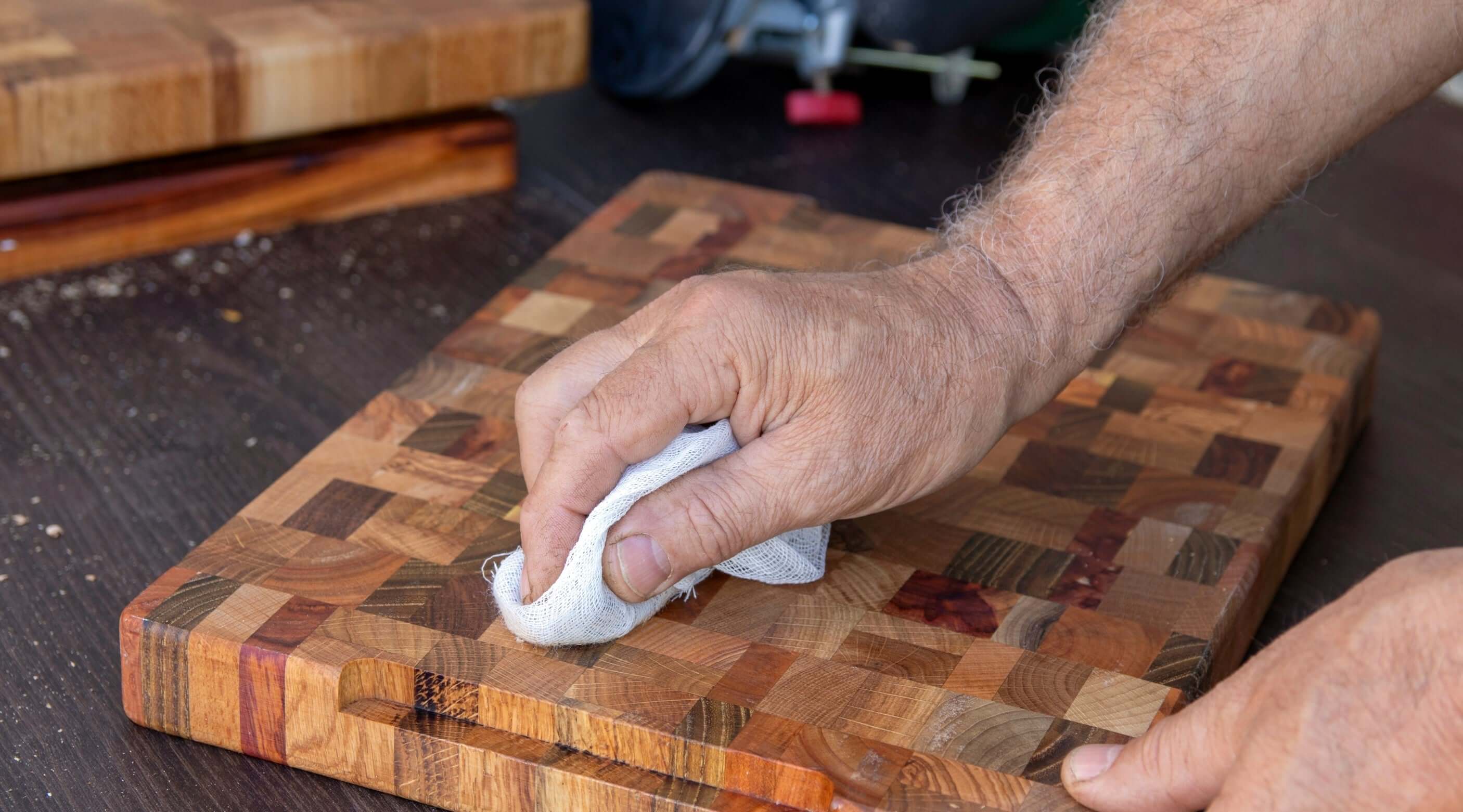 A person applying food safe oil to a wooden cutting board with a cloth, enhancing its natural beauty.