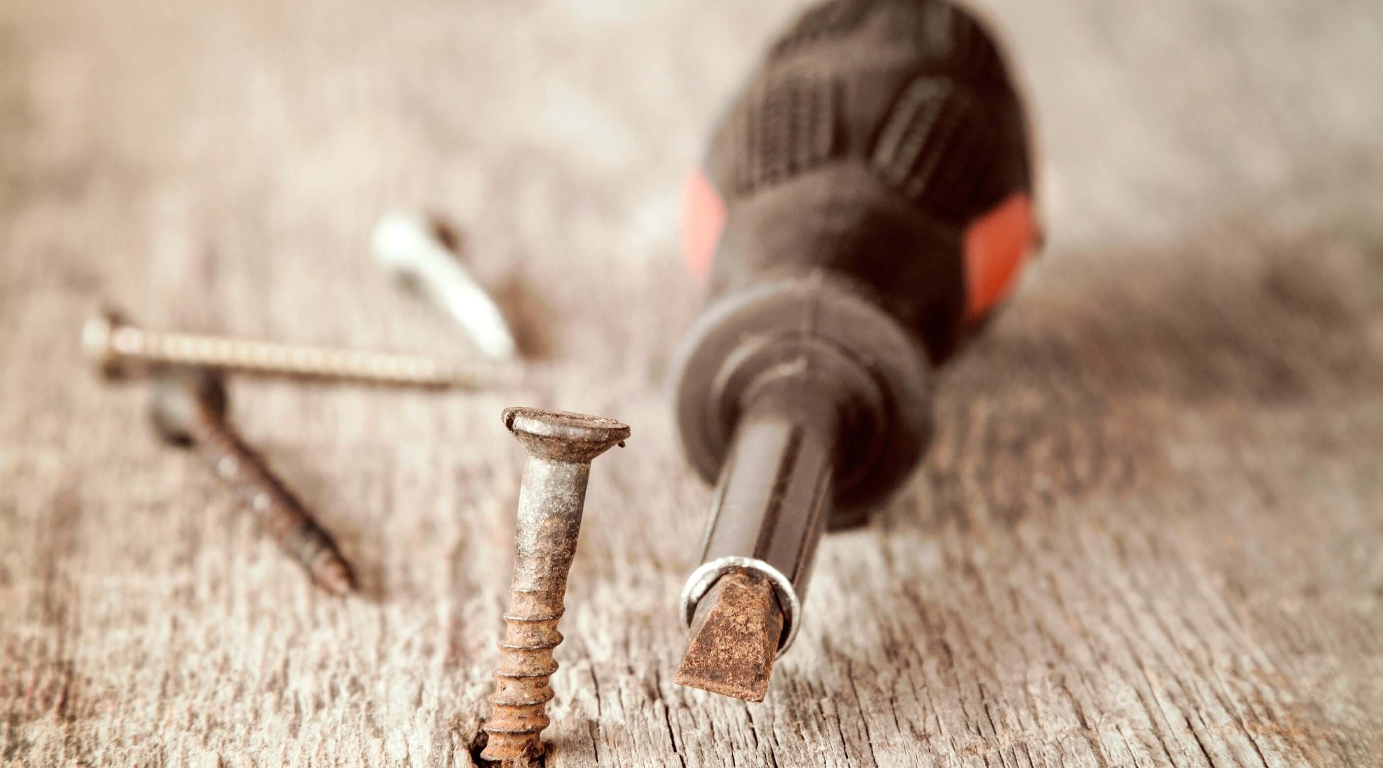 Close-up of a screwdriver and various screws on a wooden surface, highlighting essential tools for assembly and repairs.